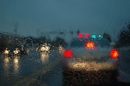 Red car break lights shown through a rainy windshield.